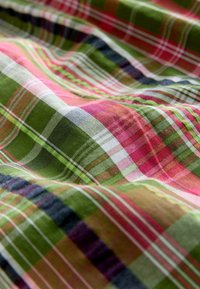 Tissu à motifs écossais avec des carrés verts vifs, roses et bleu marine. Le matériau semble léger avec une texture lisse et des détails de couture visibles.