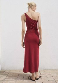 Rochie maxi roșie, cu un singur umăr, realizată dintr-un material neted, ajustată la talie și curgând până la glezne, cu un design minimalist.