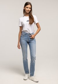 Jasnoniebieskie dżinsy z prostą nogawką, w połączeniu z białym t-shirtem z ciemnoniebieskim logo oraz białymi trampkami.