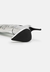 Stříbrná lodička na vysokém podpatku s elegantním designem, špičatou špičkou, hladkou kovovou texturou a černou gumovou podrážkou, zvýrazněná lesklým lemem.