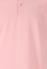 Rosa pikétröja i strukturerad tyg, med en tvåknappsrad och en liten logotyp på vänster bröst.