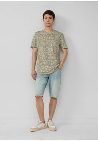 Lichtgroen gestreept t-shirt, denimshorts en witte sneakers met beige accenten. Het shirt heeft een botanische print in een vierkante indeling.