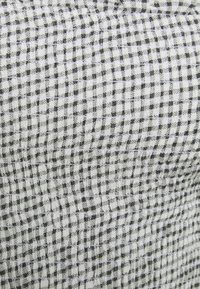 Zwart-wit geruit stof met een gestructureerd oppervlak, met een rasterpatroon van afwisselende vierkanten en een licht gekreukeld uiterlijk.