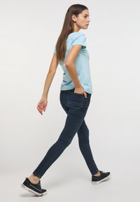 Camiseta de manga corta azul claro combinada con jeans ajustados azul oscuro. El modelo lleva zapatillas negras con suelas blancas, que presentan un diseño limpio.