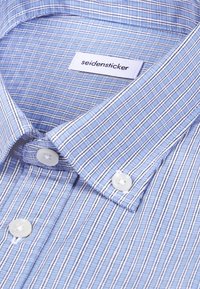 Chemise à carreaux bleu et blanc avec des boutons blancs et une étiquette « seidensticker » à l'intérieur du col.