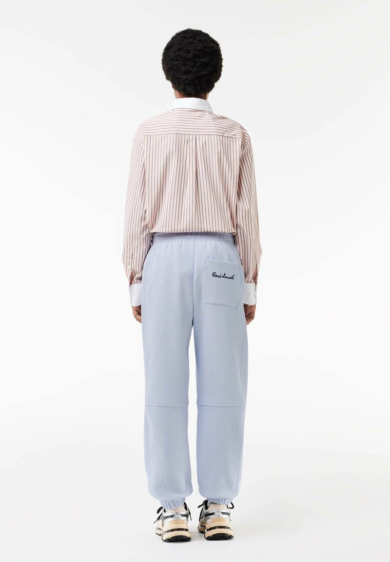 Camisa de manga larga a rayas y pantalones de chándal azul claro con puños elásticos, que presentan un bolsillo trasero con texto bordado. Fondo neutral.