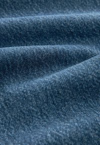 Tecido de jeans de culoare albastru închis, având o textură netedă și un model de țesătură faină vizibil, cu variații ușoare în adâncimea culorii și umbre.
