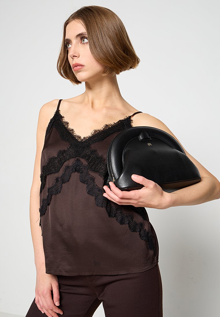 Schwarze Lederhandtasche mit abgerundeter Form, ausgestattet mit einem Reißverschluss oben und einem kleinen Akzent. Das Model trägt ein dunkles Satin-Camisole mit Spitzenverzierungen.