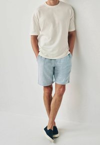 Lehký krémový tričko, uvolněný střih, kombinované se světle modrými lněnými kraťasy a námořnickými slip-on botami s bílými podrážkami. Jednoduchý design, bez vzorů.