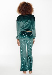 Ensemble de pyjama en velours vert avec manches longues et pantalon à jambes larges, décoré de pois blancs, texture douce et design décontracté.
