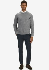 Grijze gebreide trui met ronde hals, gedragen over een witte blouse met kraag. Gecombineerd met marineblauwe broek en bruine suède schoenen.