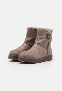 Bottines en daim marron avec une finition brillante, doublure en fausse fourrure et un accent de bouton sur le côté. Semelle en caoutchouc épaisse avec un motif de traction.