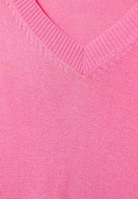 Tissu en tricot rose avec un col en côtes en V et un détail subtil de points en relief le long de l'encolure.