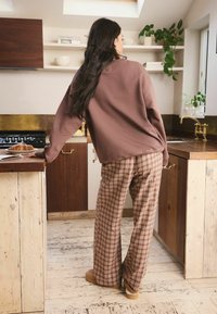Brauner, übergroßer Sweatshirt und karierte Hose in warmen Tönen. Strukturierte Holzschränke und helle Böden, mit einem gebackenen Artikel auf der Arbeitsplatte.