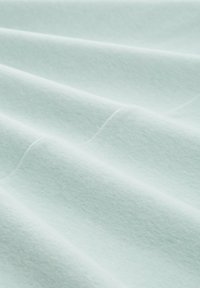 Helles mintgrünes Gewebe mit einer weichen, strukturierten Oberfläche, die sanfte Falten und Wellen zeigt, was auf ein leichtes, anpassungsfähiges Material hinweist.