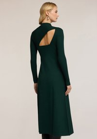 Abito a maniche lunghe, aderente, in tessuto a coste di colore verde scuro, con un dettaglio a taglio sul retro e un orlo svasato.