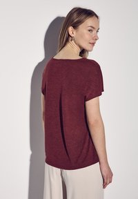 Kortærmet, kastanjefarvet T-shirt med en afslappet pasform, rund hals og subtil tekstur; parret med lyse, vide bukser.