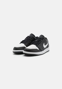 Black and white leather sneakers with a low-top design, perforated toe box, flat laces, and a white Nike swoosh on the side.