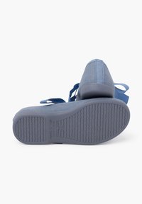 Zapatos de textil azules con parte superior texturizada, suelas de goma planas y correas azules. La vista inferior muestra un patrón de banda de rodadura y detalles de marca.
