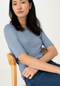 Ljust blått åtsittande t-shirt med kort ärm och rund halsringning, bärs tillsammans med mörka denimjeans. Enkelt mönster, slät textur.