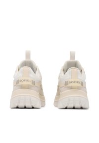 SOREL-tennarit, joissa on kermaisen värinen päällinen teksturoiduilla yksityiskohdilla, tukeva valkoinen pohja ja vetokahva takana.