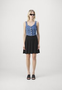 Farmer nadrág cropped top gombokkal, fekete bővülő szoknyával és fekete papucsos szandállal párosítva. A modellen sötét napszemüveg van.