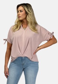 Jasnoróżowa, luźno dopasowana bluzka z dekoltem w serek i krótkimi rękawami, z trokami przy mankietach. Miękka tkanina z drapowanym przodem.
