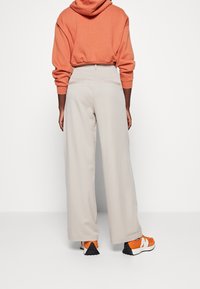 Ljusgrå vida byxor i kombination med en orange kort hoodie och orange sneakers. Slät textur, elassisk midjeresår och minimal detaljer.