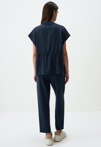 Haut léger bleu marine à manches courtes, taille cintrée, assorti à un pantalon tapered et des baskets blanches avec des accents beiges.