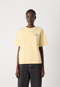 T-shirt en coton jaune clair à manches courtes avec un col rond et un logo vert en détail sur la poitrine gauche. Coupe décontractée.