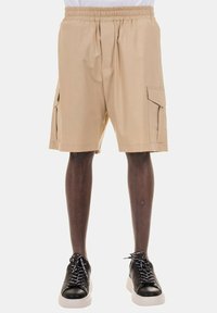 Pantaloni cargo beige con vita elastica, due tasche laterali e una trama di tessuto liscia, abbinati a scarpe da ginnastica nere con lacci bianchi.