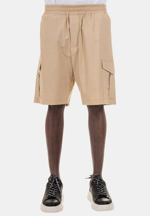 Pantaloni cargo beige con vita elastica, due tasche laterali e una trama di tessuto liscia, abbinati a scarpe da ginnastica nere con lacci bianchi.