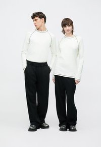 Biele košele s dlhým rukávom s kontrastným prešívaním v kombinácii s voľnými čiernymi nohavicami. Topánky sú tmavé s elegantným zaobleným dizajnom.