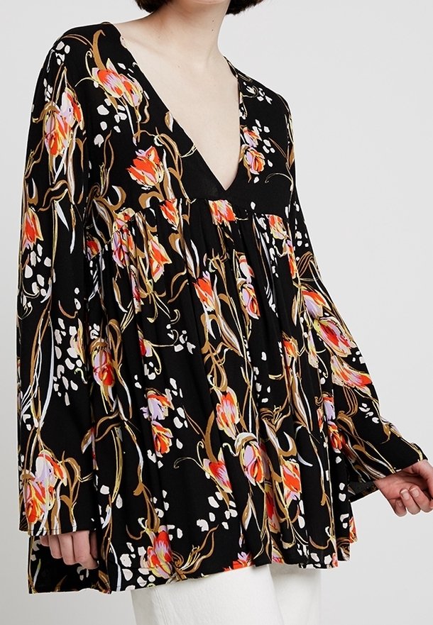 Blouse noire à fleurs avec un profond décolleté en V, manches longues, imprimés colorés de tulipes en orange et violet, partie inférieure froncée, tissu léger.