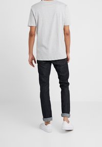 Grijs katoenen T-shirt gecombineerd met donkere denim jeans met omgeslagen pijpen en witte sneakers, gezien vanaf de achterkant.