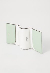 Portefeuille plié en cuir vert menthe et blanc avec une texture lisse, doté d'une fermeture à pression en argent et d'un logo embossé à l'intérieur.