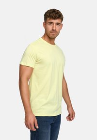 Helles gelbes Kurzarm-T-Shirt mit Rundhalsausschnitt. Weicher Baumwollstoff, figurnahe Passform, mit einem kleinen Logo auf der linken Brust.