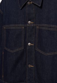 Tmavomodrá rifľová bunda spredu s dvoma veľkými vreckami na prsiach, hnedým kontrastným prešívaním a striebornými kovovými cvokmi.