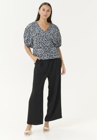 Un pantalon large noir associé à une blouse ample à motifs avec un design abstrait blanc et bleu et un décolleté en V.