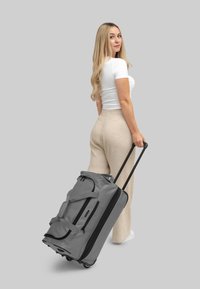 Borsa da viaggio grigia con dettagli neri, dotata di ruote robuste, doppie maniglie e una tasca anteriore con cerniera; realizzata in tessuto resistente.