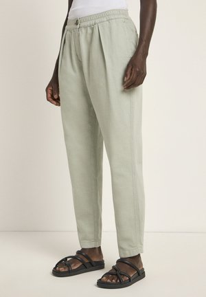 Light green trousers with a relaxed fit, elastic waistband, and side pleats; paired with black strappy sandals. Smooth fabric texture.