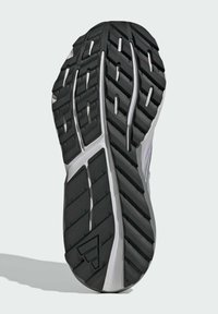 Black rubber shoe sole with multi-directional tread pattern, featuring grooves and ridges for traction. Silver accent near the heel.