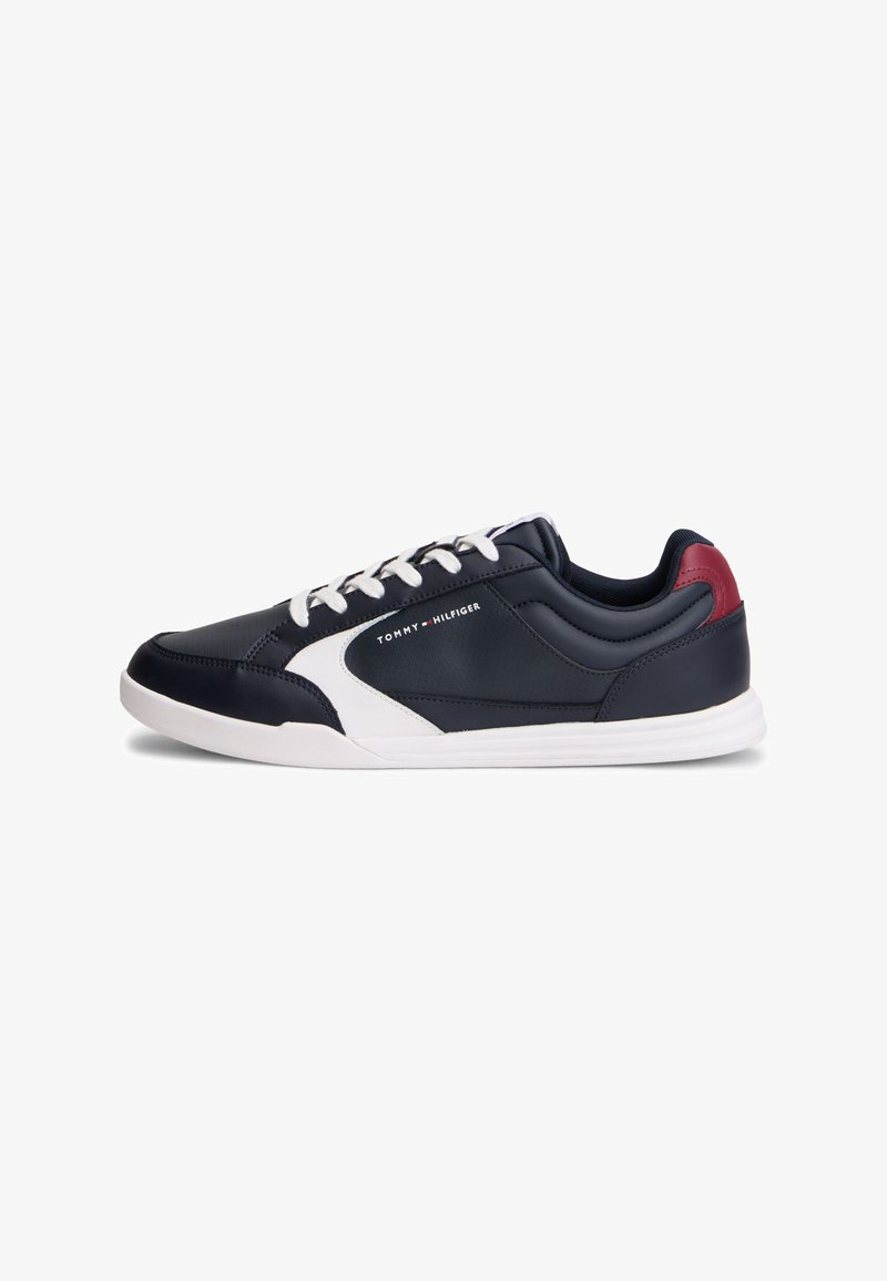 Baskets bleu marine avec semelle blanche, accent latéral blanc, patch rouge au talon, lacets blancs et logo "Tommy Hilfiger" sur le côté.