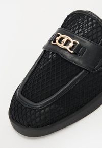 Sorte slip-on sko med en mesh-overdel med diamantmønster, læderdetaljer og en guldfarvet kædedesign på remmen.