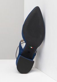 Blaue Wildledersandalen mit Absatz, spitzer Zehenform, schrägem Absatz und Gummisohle mit strukturiertem Grip. Markenname und Herkunftsland sind gekennzeichnet.