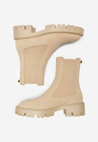 Bottines beiges avec une finition en cuir lisse, des panneaux latéraux élastiques et des semelles crantées pour une meilleure adhérence. Design minimaliste avec des textures contrastées.