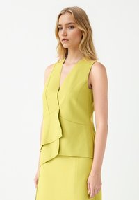 Mouwloos geel topje met een diepe V-hals, gelaagd ontwerp en gestructureerde plooien. Gemaakt van gladde stof, heeft het een getailleerde pasvorm en strakke lijnen.