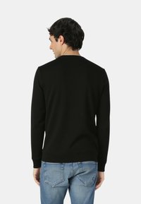 Maglione nero a maniche lunghe con scollo rotondo. Realizzato in un tessuto liscio, presenta polsini e orlo a coste, indossato con jeans azzurri.