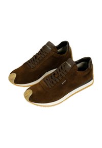 Sneakers in suede marrone con design a lacci, suola intermedia bianca e suola in gomma naturale. Presentano un tessuto texturizzato e un logo discreto sulla linguetta.
