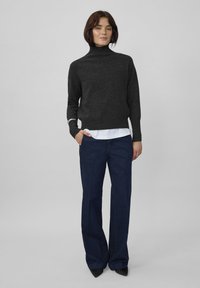 Tumši pelēks augsta apkakle džemperis biezā adījumā, apvienots ar brīviem tumši ziliem džinsiem. Džemperim ir ribotas rokavi un apakšmala, ar baltu kreklu zem tā.